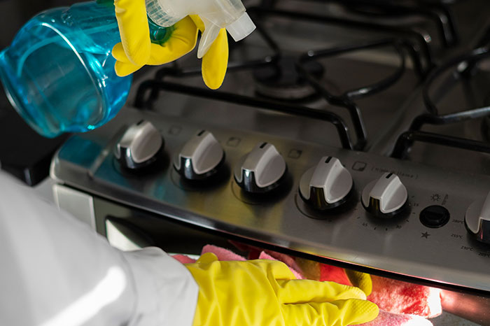 Persona limpiando con productos químicos unos fogones de cocina.